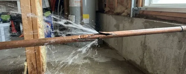 Burst copper pipe spraying water in a basement along a concrete foundation wall